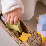 Hand reaching for Pastel Geometric Figures Floating Stacking Blocks in Natural Rubber box