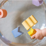 Yellow sponge held above a clear container with Pastel Geometric Figures in Natural Rubber