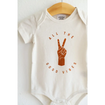 White baby onesie in organic cotton with orange Good Vibes text and peace sign graphic