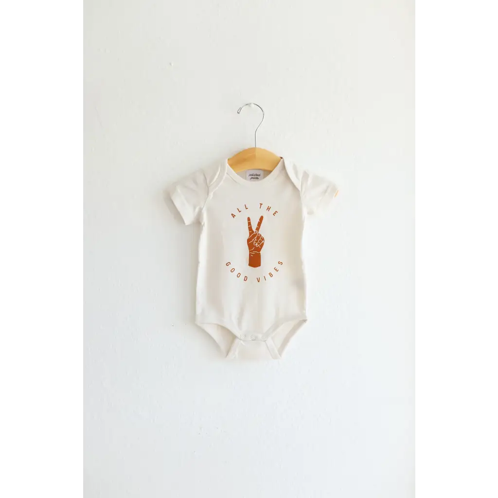 White baby onesie in organic cotton with brown peace sign graphic for good vibes organic style