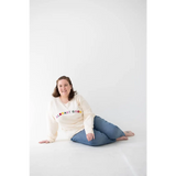 Person in cream embroidered organic cotton sweatshirt and blue jeans sitting on floor
