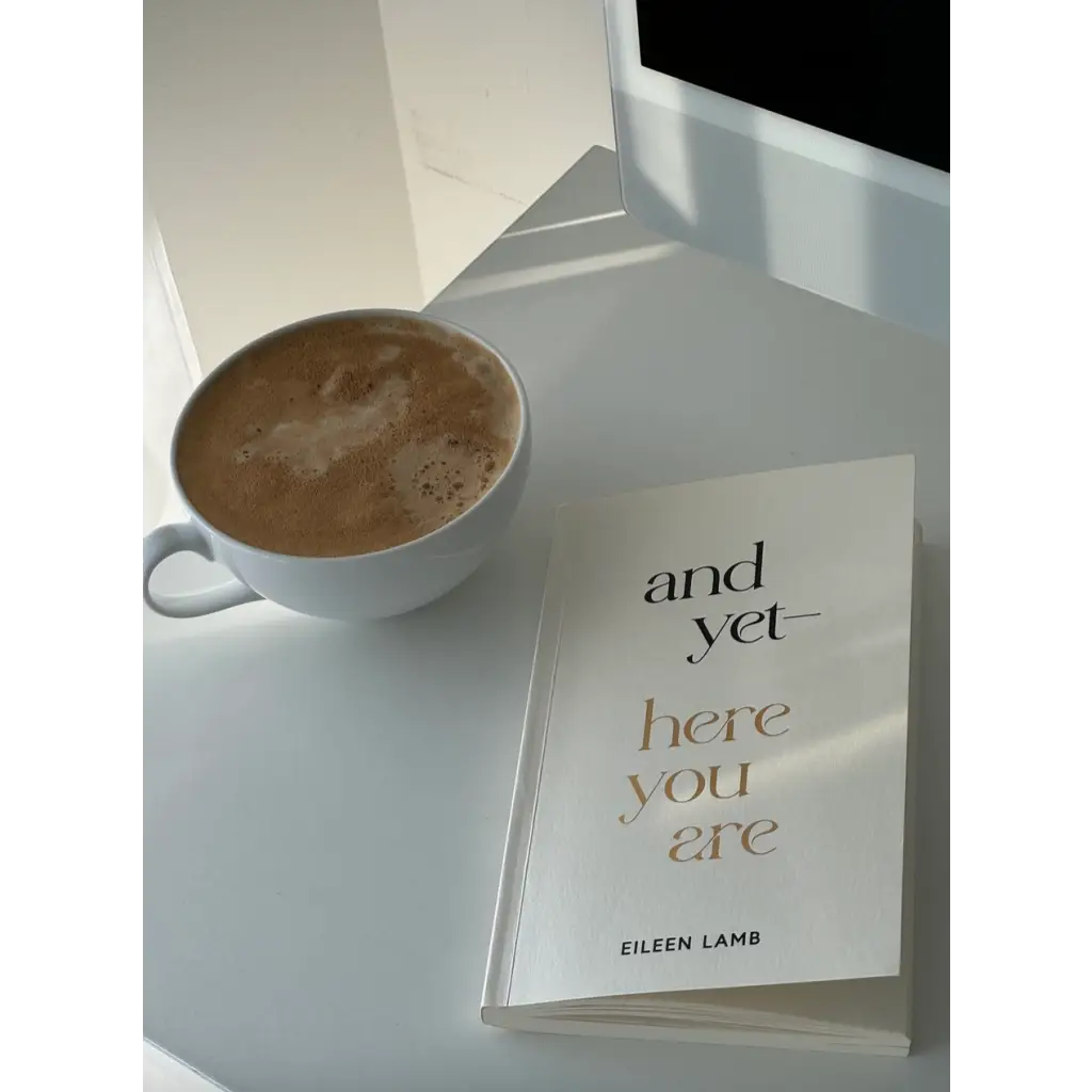 Cozy white cup of hot chocolate with Eileen Lamb’s And Yet Here You Are book, Edwardsville