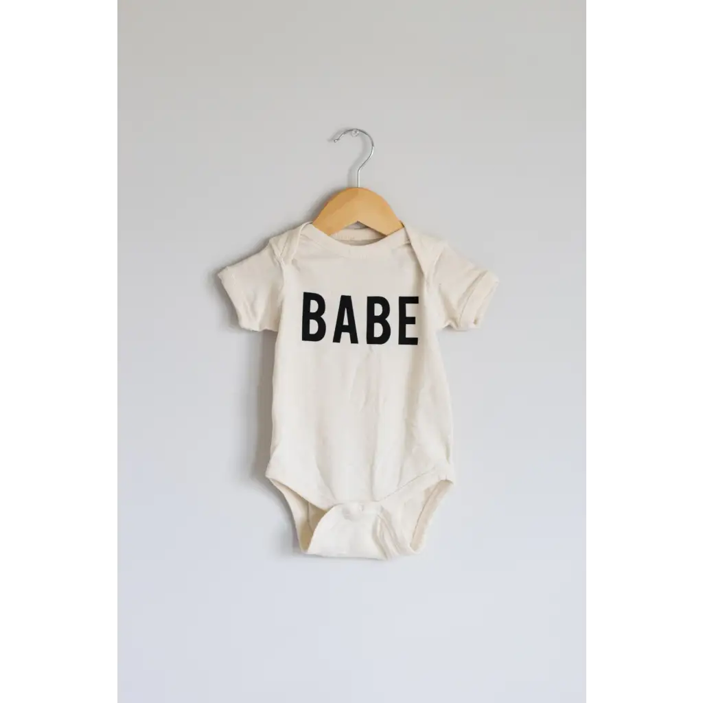 White baby onesie made of organic cotton fabric with Babe printed in bold black letters