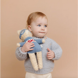 Baby in gray knit sweater holding Benjamin Bear Ski Plushie, ready for snow adventures