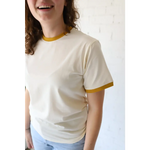 Cream-colored organic cotton women’s ringer tee with mustard trim and polished prints