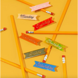 Colorful ribbon-shaped labels for the week with gold alligator clips and cursive ink inlay