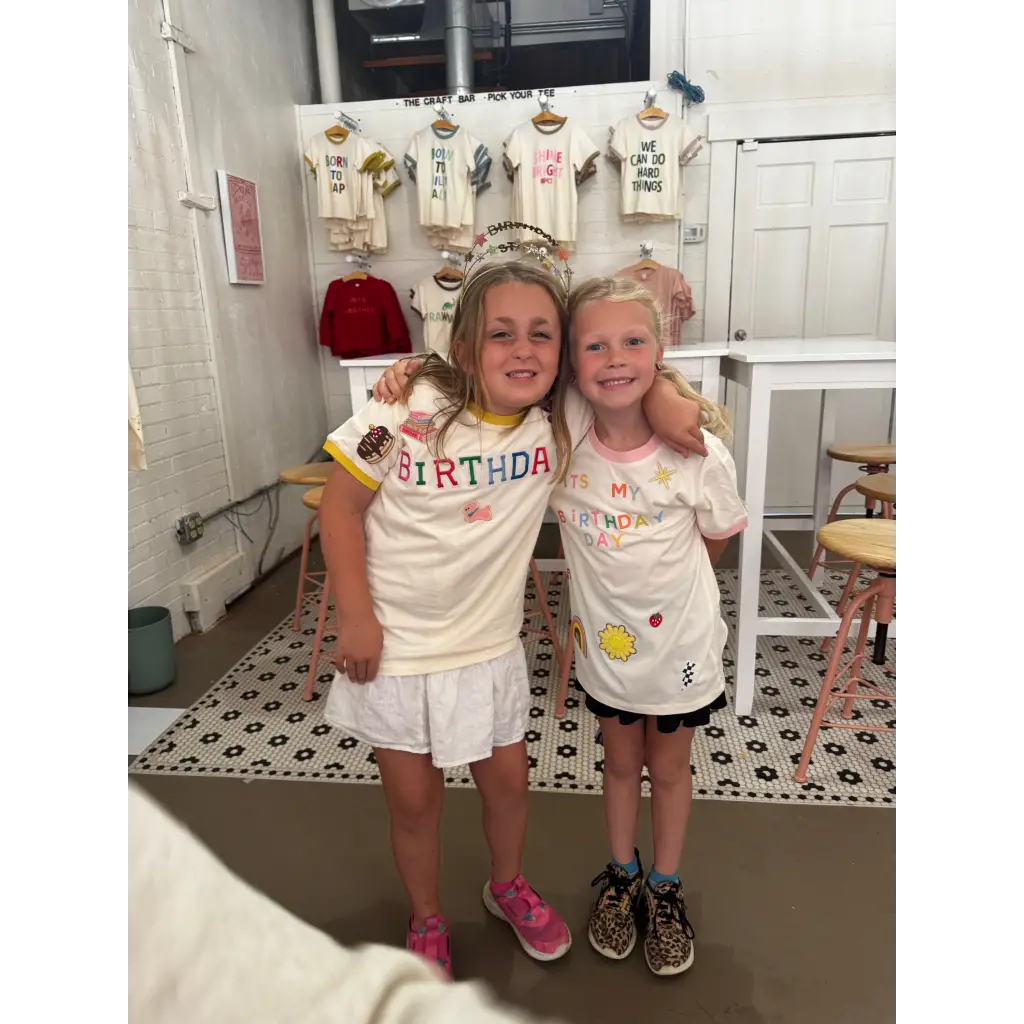 Two happy girls in birthday-themed shirts at the craft bar with a fun bar host