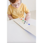 Young kid in yellow shirt with watercolor book and colorful prints, holding a brush pen
