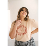 Beige Empowered Women graphic t-shirt with red design, styled with a checkered skirt