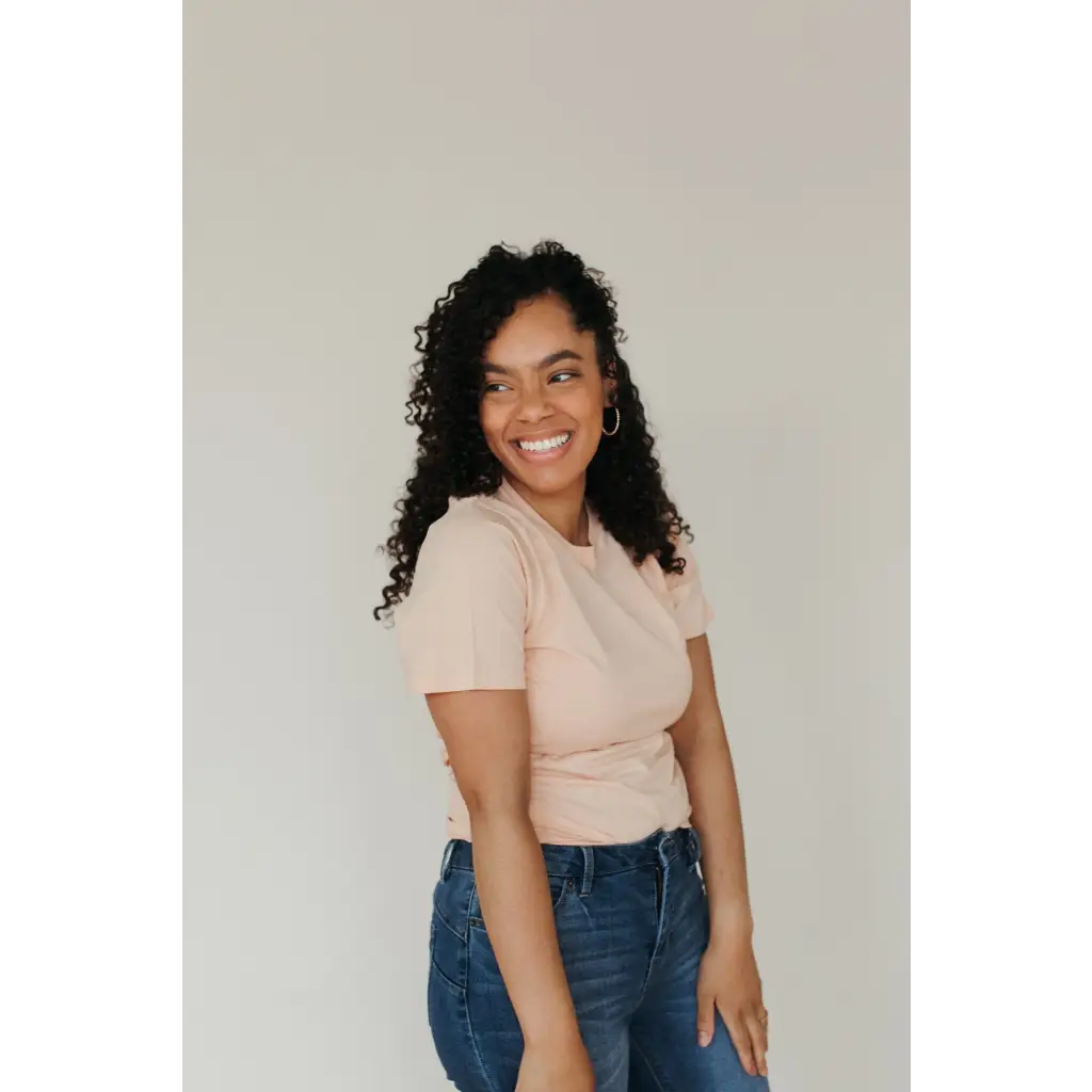 Smiling person in a beige Peach Unisex Adult Tee made with organic cotton and blue jeans