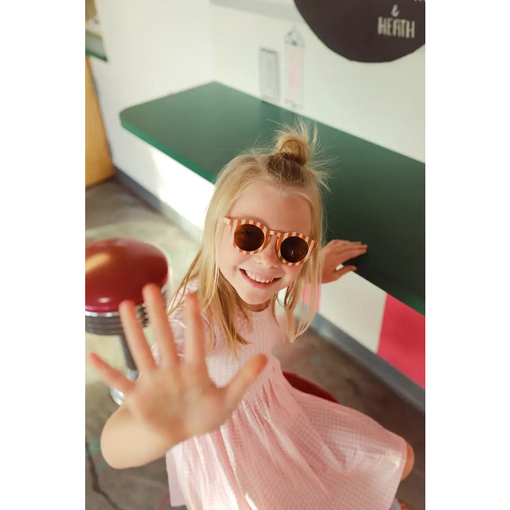 Playful kid in pink sunglasses and shirt showcasing the Gingham All Day Twirl Dress