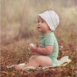 Baby in a white bonnet and green striped onesie with Estella Organic Baseball Rattle