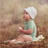 Baby in a white bonnet and green striped onesie with Estella Organic Baseball Rattle