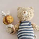 Henry Bear in a cozy striped shirt happily holding a cute crocheted bee toy