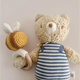 Henry Bear in a cozy striped shirt happily holding a cute crocheted bee toy