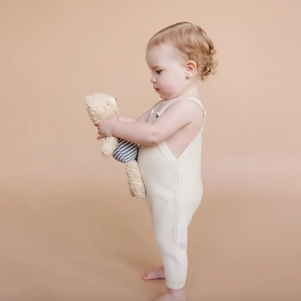 Toddler in cream romper cuddling teddy bear from Henry Bear Loves Spending Time line