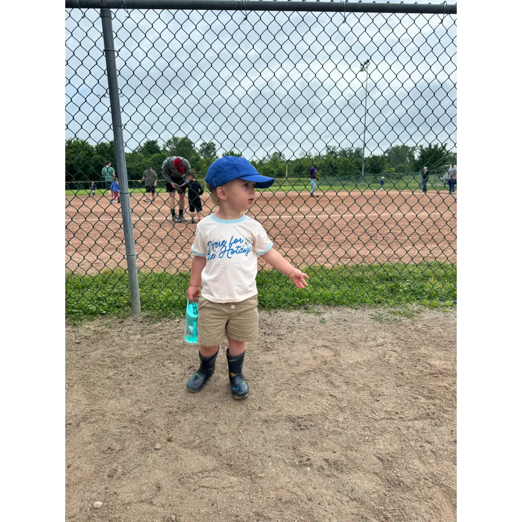 Toddler in baseball cap on field rocking Here for the Holidays Brutally Honest Tee in Organic Cotton