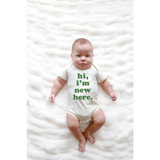 Baby wearing a Hi I’m New Here Baby Onesie in Organic Cotton Sage with green text