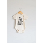 White organic cotton baby onesie with Hi, I’m New Here print in black letters