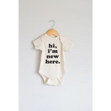 White organic cotton baby onesie with Hi, I’m New Here print in black letters
