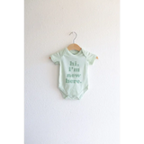Mint green organic cotton baby onesie with hi, I’m new here text on wooden hanger
