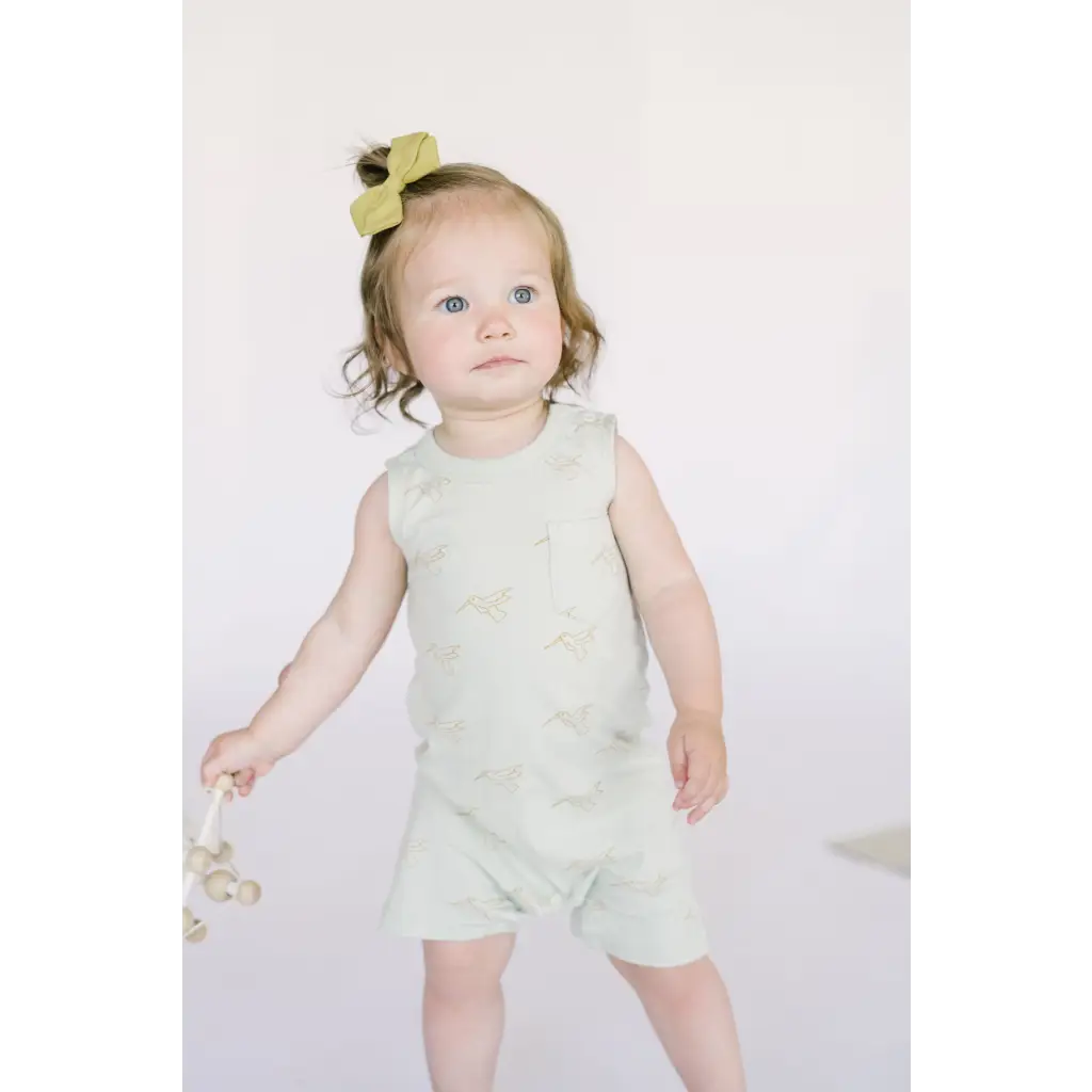 Toddler in mint green Hummingbird Pocket Playsuit with yellow hair bow, perfect one-piece
