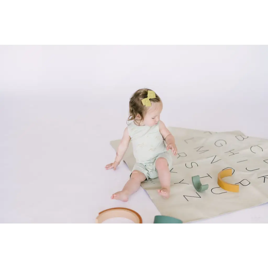 Baby enjoying the Hummingbird Pocket Playsuit on a colorful alphabet play mat