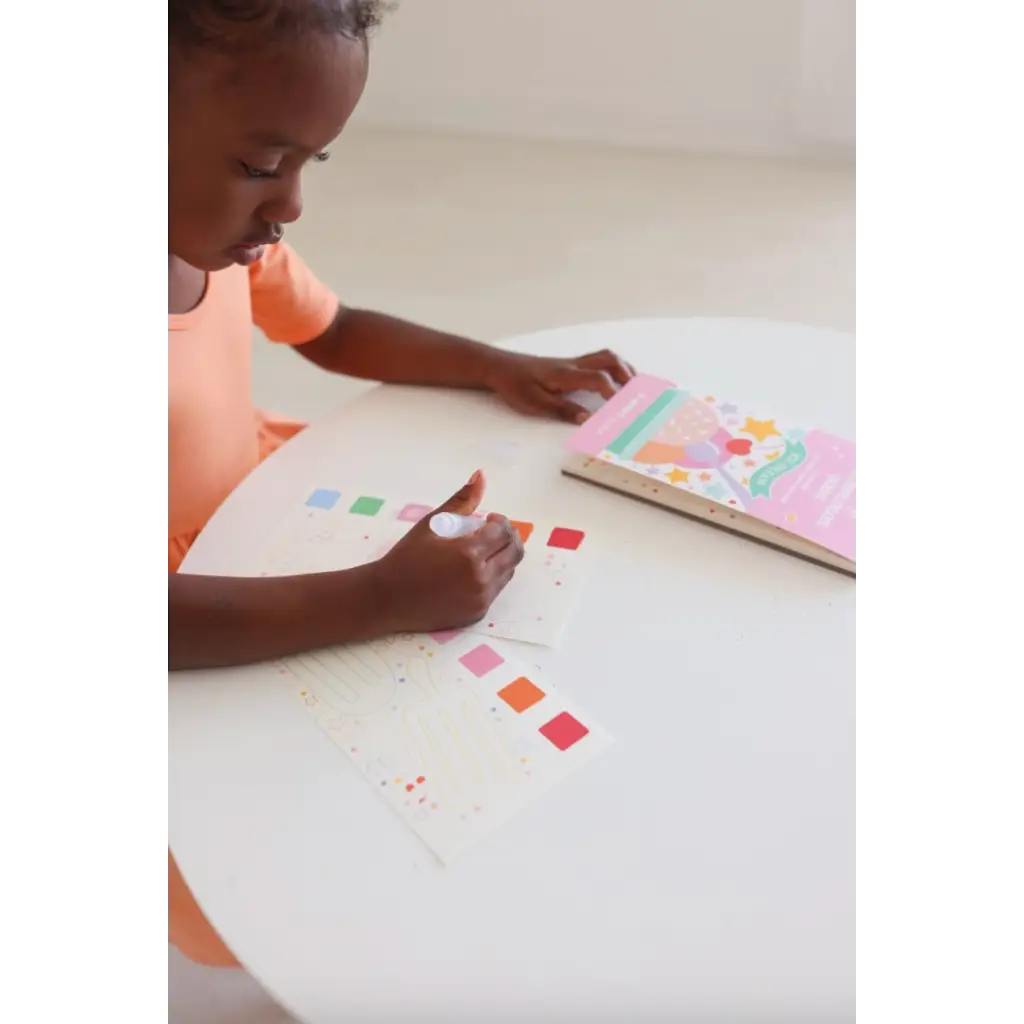 Young kid with dark skin coloring in Ice Cream Pocket Watercolor Book at a white table