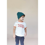 Child in a white ringer tee, blue jeans, and teal beanie rocking stylish vibes