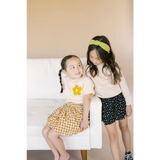 Two kids in patterned skirts on a chair, wearing love grow graphic t-shirts