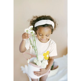Child in white clothes holding flowers with Let Love Grow Graphic T-shirt for Kids
