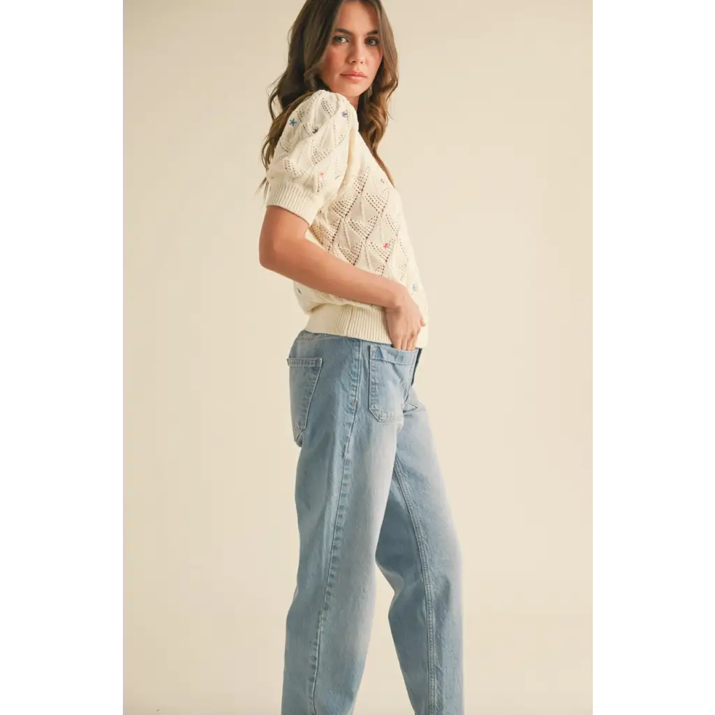 Woman in cream pointelle knit sweater with floral embroidery and light-wash jeans