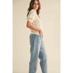 Woman in cream pointelle knit sweater with floral embroidery and light-wash jeans