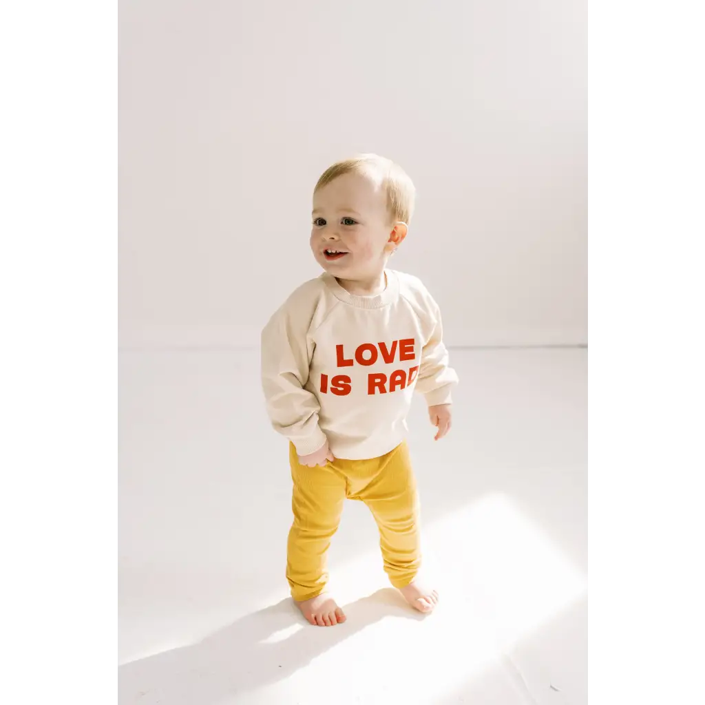 Toddler in a white LOVE IS sweater and yellow pants with a rad baby pullover look