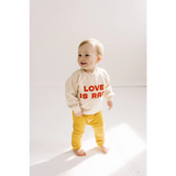 Toddler in a white LOVE IS sweater and yellow pants with a rad baby pullover look