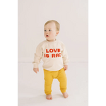 Toddler in cream Love Is Rad baby pullover sweatshirt and yellow pants, made of organic cotton fabric