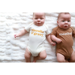 Two babies in stylish organic cotton onesies with polished prints saying biscuits n’ gravy and meatball