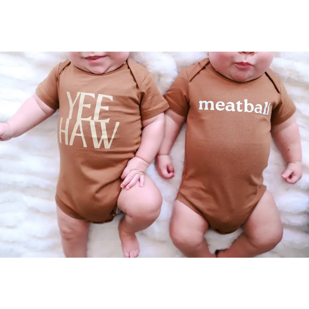 Two brown organic cotton baby onesies with polished prints YEE HAW and meatball designs