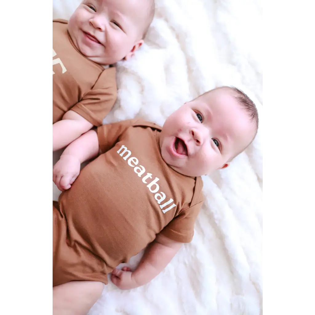 Two smiling babies in matching brown Meatball Organic Cotton Baby Onesies with stylish polished prints