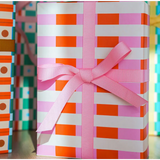 Gift-wrapped package in orange and white striped Merengue wrapping paper with pink bow