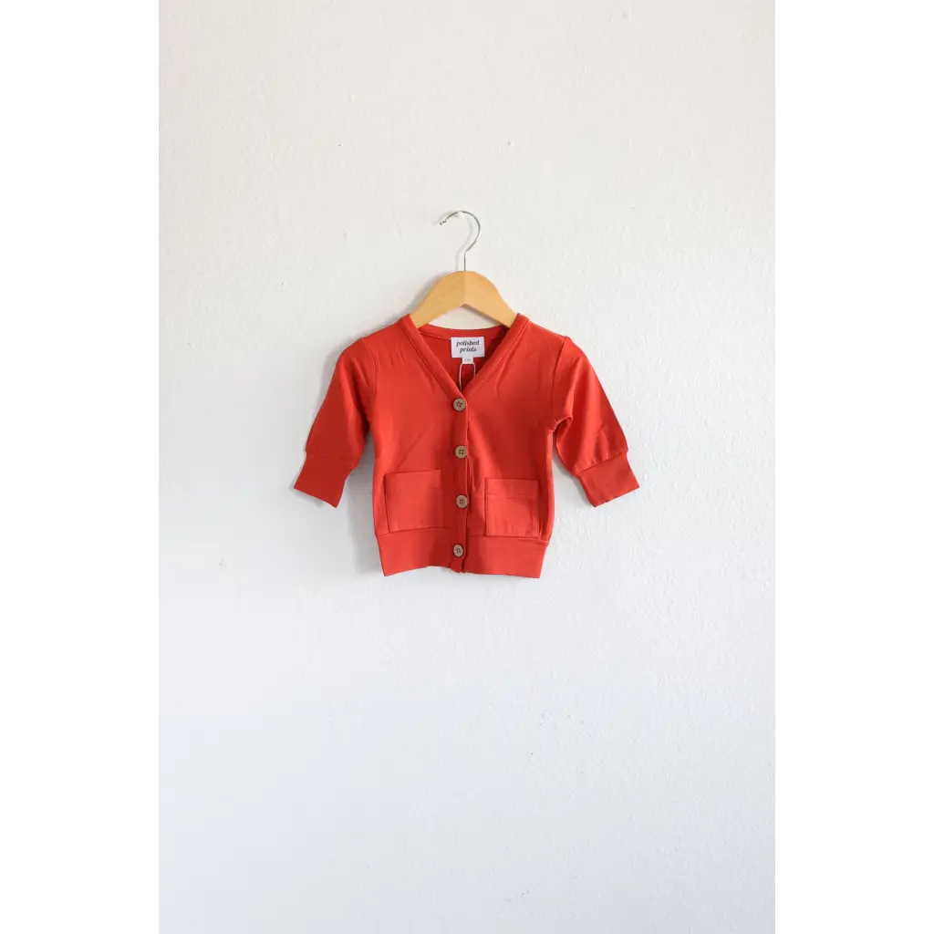 Buttery soft red mini grandpa cardigan sweater on a wooden hanger for the holiday season