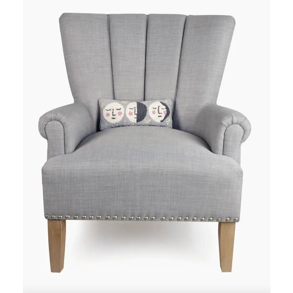Gray upholstered armchair showcasing a hooked accent pillow with velvet backing