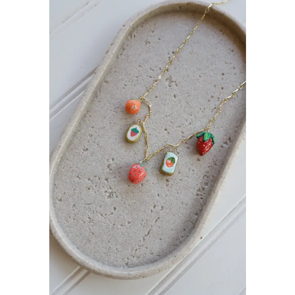 Gold chain necklace with colorful fruit-themed clay charms on a seaside charm necklace