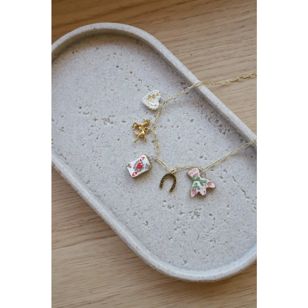 Gold seaside charm necklace with clay charms like a heart, horse, card, horseshoe, and dress