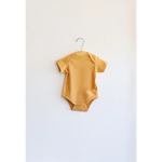 Yellow Oak Bluff baby bodysuit hanging on a hanger, made from organic cotton