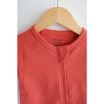 Coral Organic Cotton Baby Zipper Sleeper hanging on a wooden hanger for cozy comfort