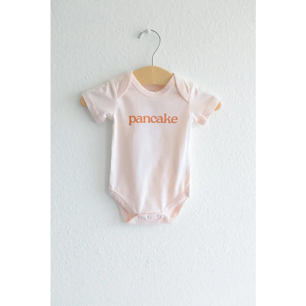 Light Pink Pancake Organic Cotton Onesie featuring orange pancake text for cozy cuties