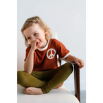 Giggling kid in rust Peace Embroidered Ringer Tee and olive pants, perfect for everyday fun