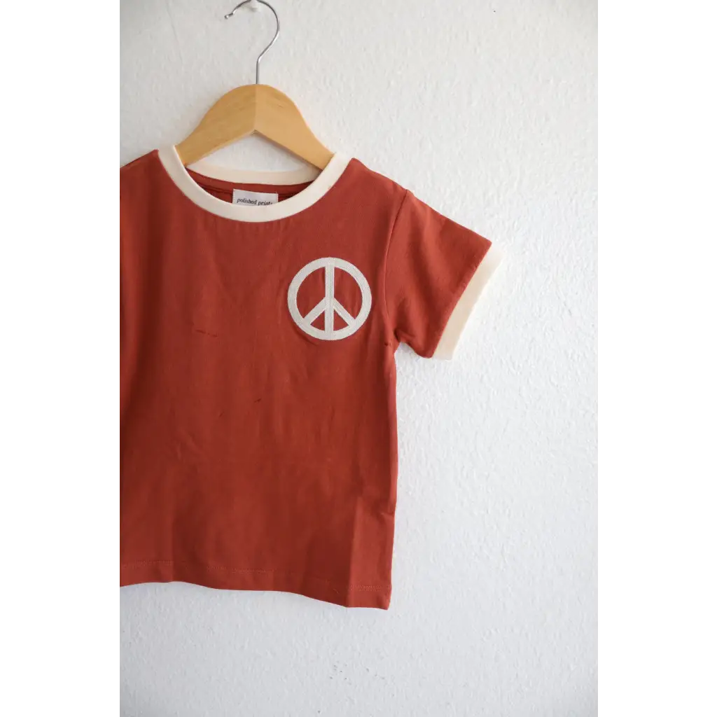 Rust Peace Embroidered Ringer Tee for Kids hanging on a wooden hanger, perfect everyday ringer