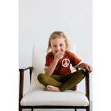 White upholstered chair with wooden armrests next to a kids Peace Embroidered Ringer Tee